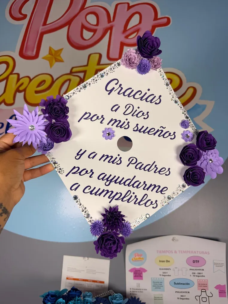 Birrete de graduación blanco con flores moradas y mensaje en español